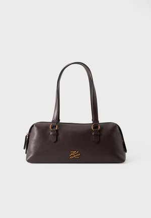 Sac à main en cuir marron foncé avec deux poignées et un petit logo doré à l'avant, sur fond blanc.
