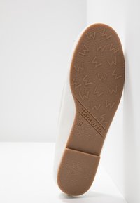 Semelle d'une chaussure blanche avec une semelle en caoutchouc marron texturée, présentant un motif W répété, nom de la marque Tamaris et indication de la taille 37.