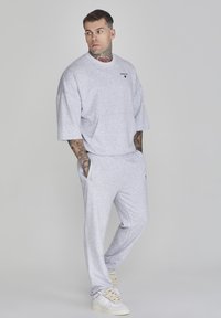 Siva oversized dukserica i odgovarajuće donje hlače od mekanog materijala. Ima prednji dzep i bočne dzepove. Nosite sa bijelim tenisicama.