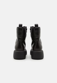 Stivaletti alla caviglia in pelle nera con suola robusta, zip laterali e linguette posteriori. Texture liscia e dettagli di design minimalisti.