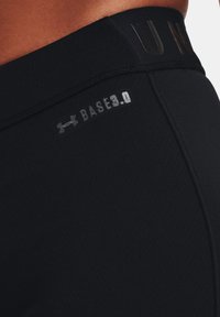 Zwarte sportleggings met een soepele textuur, een elastische tailleband met het reliëf van "UNDER ARMOUR" en "BASE 3.0" branding in zilveren details.
