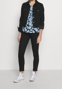 Giacca in denim nera, blusa floreale blu con accenti verdi, jeans skinny neri e sneakers bianche alte. Outfit semplice e casual.