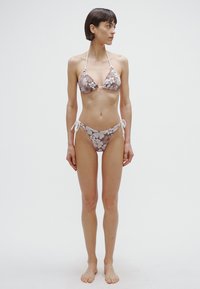 Brown floral print bikini featuring a triangular top with thin straps and a matching bottom with side ties; smooth fabric, minimal coverage.