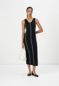 Black knitted dress with white vertical stripes, sleeveless design, knee-length, paired with a white textured bag and black flats.