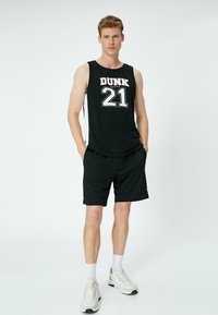 Sort atletisk tanktop med "DUNK 21" trykt i hvid og rød. Paireret med sorte shorts og lyse sneakers. Enkel design.