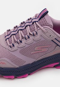 Baskets de sport lilas clair avec un tissu en maille, des superpositions texturées, une semelle contrastante violette foncée et des accents roses. Équipées de lacets élastiques et d'un détail de logo.