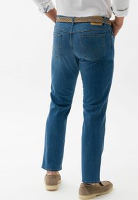 Jeans in denim blu scuro con vestibilità slim, dotati di una cintura intrecciata color tan, cuciture discrete sulle tasche posteriori e un design a gamba dritta.