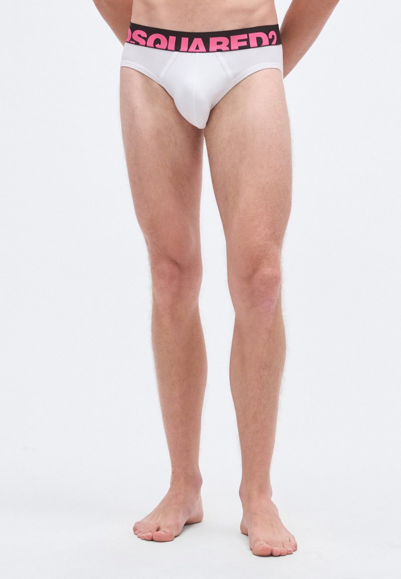 Calzoncillos blancos para hombre con una cintura negra que presenta el logo rosa "DSQUARED2". Los calzoncillos tienen una textura suave y un ajuste ceñido.