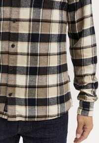 Geruit flanellen overhemd in beige, bruin en navy kleuren. Heeft knopen aan de voorkant, lange mouwen en de typische textuur van flanellen stof.