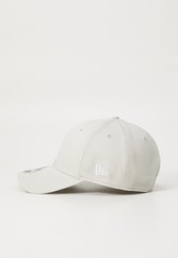 Beige színű baseball sapka, textilből készült, ívelt karimával és hímzett logóval az elején és az oldalon. Texturált felület, hátul állítható pánt.