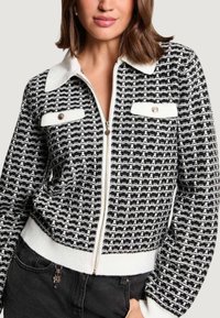 Giacca con zip a motivo bianco e nero, colletto con risvolto e tessuto strutturato, con tasche con zip e polsini a coste.