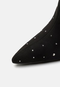 Stivaletto in suede nero con punta appuntita e decorazioni di strass sparse. Texture liscia impreziosita da dettagli lucidi e riflettenti.