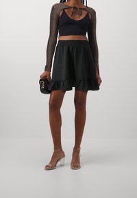 Černý zkrácený top s dlouhými rukávy s kovovými akcenty, doplněný černou nabíranou sukní. Celý outfit doplňují sandály s transparentním podpatkem.