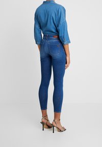 Jeans skinny de mezclilla azul de cintura alta, con bolsillos traseros y una textura suave. Combinados con sandalias de tacón alto con tiras.