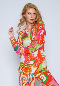 Farbenfrohes Loungewear-Set mit einem lebhaften Blumen- und Wirbelmuster in Pink, Grün und Orange, aus leichtem Stoff gefertigt.