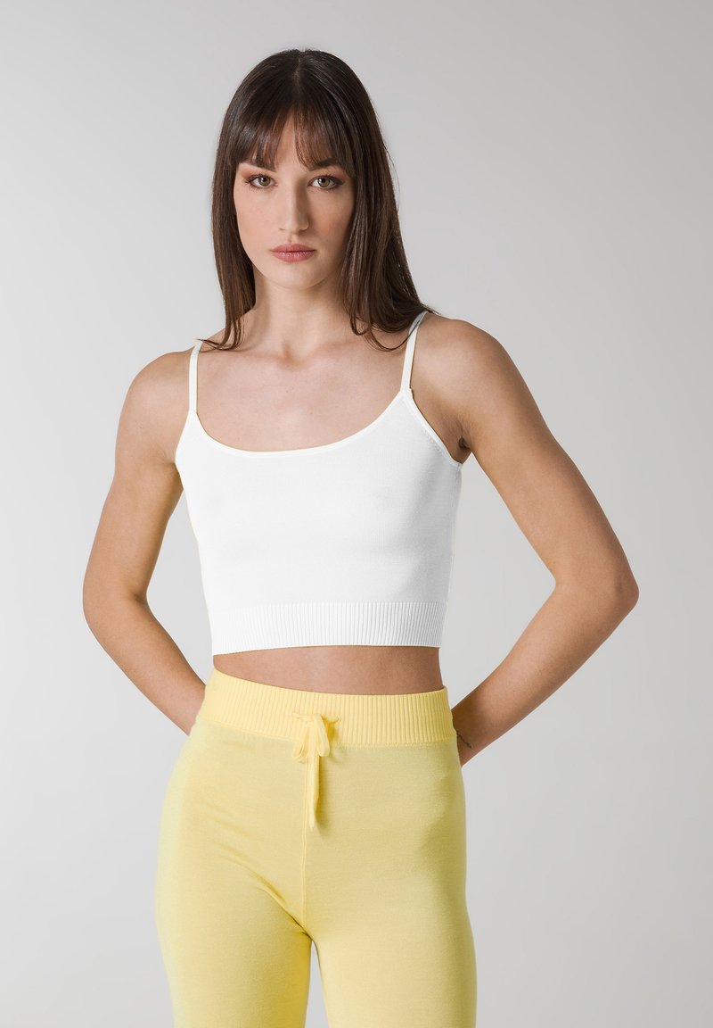 Top corto blanco con textura de canalé y tirantes finos, combinado con leggins amarillos de cintura alta y cordón. Tejido simple y elástico con un ajuste ceñido.