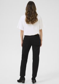 Jean en denim noir avec une silhouette ajustée, dotés de poches arrière et d'une taille mi-haute, associés à un t-shirt blanc et des talons noirs.