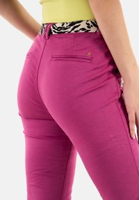 Růžové kalhoty ve fuchsiové barvě s přiléhavým střihem, vybavené zadními kapsami, leopardím potiskem na pasu a malým zlatým logem.