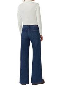 Wijde spijkerbroek in donkerblauw denim, voorzien van een hoge taille, voorzakken en achterzakken met een textuurstof. Gecombineerd met een witte top.