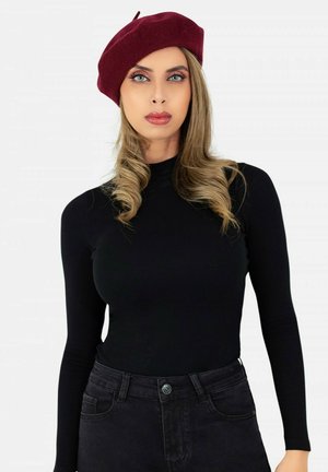 Béret bordeaux sur un modèle avec de longs cheveux ondulés. Conçu avec un haut noir à manches longues ajusté et un jean foncé, créant un look contrasté.