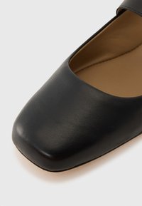 Black leather flat shoe with a square toe, smooth texture, and a slight cutout design at the sides. Inner lining is a light tan color.