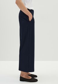 Marine wijde broek in gestructureerde stof, met zijzakken en een hoge tailleband. Gepaard met zwarte platte schoenen.