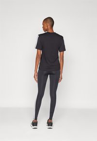 T-shirt nera a maniche corte, con accenti bianchi, abbinata a leggings neri aderenti con strisce laterali bianche.