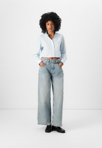Light blue cropped button-up shirt, denim wide-leg jeans, black shoes; features a tailored fit and classic design with visible stitching.