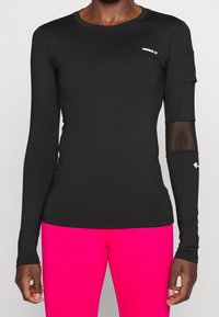 Schwarzes langärmliges Sportoberteil mit glatter Textur, ausgestattet mit einem Logo und einem Netz-Akzent am rechten Ärmel, kombiniert mit leuchtend pinkfarbenen Leggings.