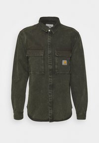 Ciemnozielona koszula dżinsowa z długimi rękawami, dwoma kieszeniami na piersi i zapięciem na guziki. Posiada naszywkę z logo na lewej kieszeni.