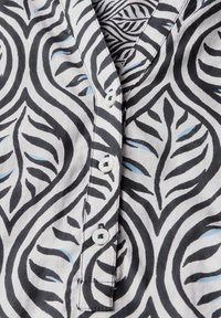 Camicia di stoffa bianca con un motivo a foglie nere e blu, con scollatura a V e cinque bottoni bianchi sul davanti.
