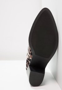 Zapato de tacón alto con estampado de leopardo, que presenta un tejido texturizado, una suela de goma negra sólida y un diseño de tacón cuadrado.
