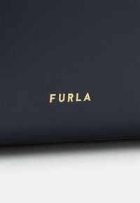 Surface noire avec texte en relief doré « FURLA » centré près du bord inférieur.