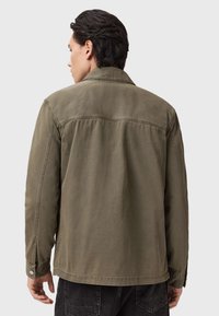 Giacca verde oliva, tessuto leggero, polsini impreziositi da bottoni, dettaglio sulla parte posteriore, taglio dritto, design casual, senza loghi o motivi visibili.