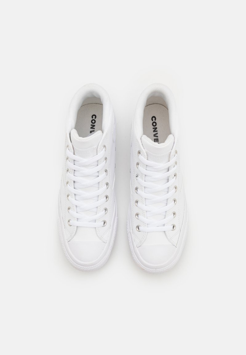 Zapatillas de lona blancas con un diseño de caña baja, que cuentan con cordones planos, ojales metálicos y una suela de goma texturizada. El logo de la marca es visible en la plantilla.