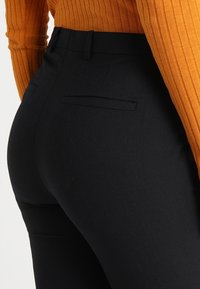 Musta räätälöity housut, joissa on sileä pinta ja slim fit -leikkaus, kahdella takataskulla ja litteällä vyötäröosalla, yhdistettynä oranssiin ribattu yläosaan.