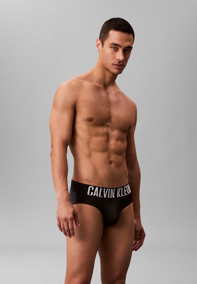 Zwarte herenboxershorts met een brede witte CALVIN KLEIN-logo tailleband, voorzien van een aansluitend ontwerp en een gladde textuur tegen de blote huid.