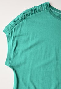 Camiseta de manga corta color turquesa hecha de tejido suave, que presenta detalles de volantes fruncidos a lo largo de la costura del hombro.