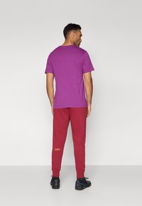 Purpura kokvilnas T-krekls ar apaļu kakla izgriezumu, apvienots ar sarkaniem sporta biksēm ar ribotu potīšu maliņu un dzelteniem apļa akcentiem tuvāk apakšai.