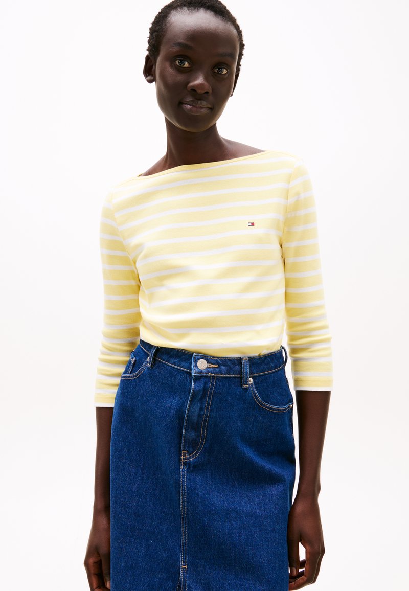 Geel en witte gestreepte long sleeve top met een boot halslijn, gecombineerd met een donkerblauwe denim rok met knopen en naden aan de voorkant.