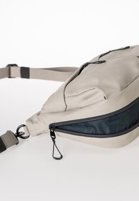 Grau textile Slingbag mit einem Reißverschlussfach, verstellbarem Gurt und schwarzen Akzenten. Strukturiertes Material, aerodynamische Form und Metallbeschläge.