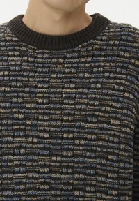 Pleteni pulover z črnimi rebrastimi robovi, večbarvno nitjo v modri, kremni in črni vzorci ter teksturirano površino.
