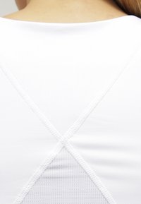 Top deportivo blanco de tirantes, con un tejido texturizado y transpirable, diseño de espalda cruzada y detalles cosidos.