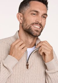 Maglione beige a vetri con collare a mezza zip, dotato di polsini a coste e tirazip in pelle marrone. Texture liscia, design leggero.