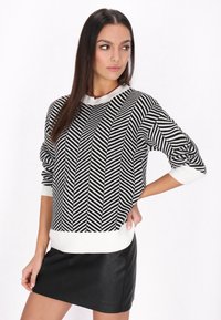 Pulover tricotat cu model chevron alb și negru, cu guler rotunjit, manșete și tiv cu dantelă, purtat cu o fustă mini din piele neagră.