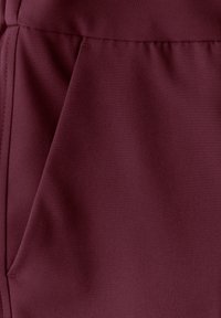 Tissu bordeaux au toucher lisse, avec une légère brillance. Comprend une couture verticale et un détail de poche sur un côté.
