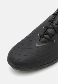 Zwarte sportieve schoen met textuur, gemodelleerd leren bovenwerk, met horizontale strepen en zwarte veters. Subtiel logo-detail nabij de tenen.