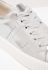 Zilveren lakleren sneaker met vlakke, gevlochten satijnen veters, decoratieve perforaties en een gestructureerde witte rubberen zool.