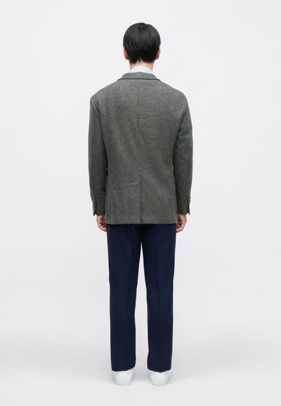 Szary wełniany blezer z klapami z wycięciem, pojedynczym rozcięciem i dwoma tylnymi kieszeniami, zestawiony z granatowymi spodniami i białymi trampkami.