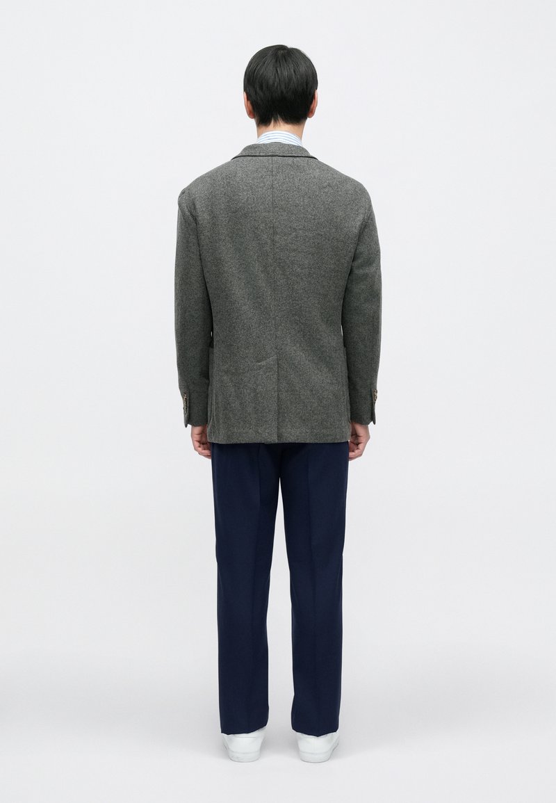 Grijze wollen blazer met ingesneden revers, enkele achtersplit en twee achterzakken, gecombineerd met marineblauwe broek en witte sneakers.